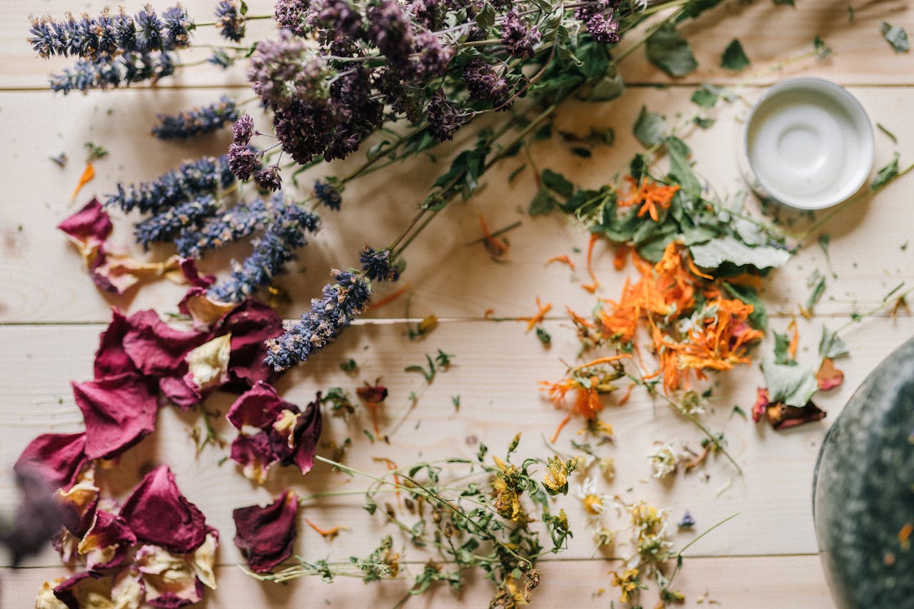 Assorted dried flowers and herbs scattered on a wooden table with a ceramic bowl.